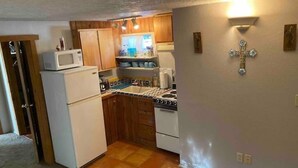 Una cocina compacta con armarios de madera, un microondas, una estufa y un lavamanos.