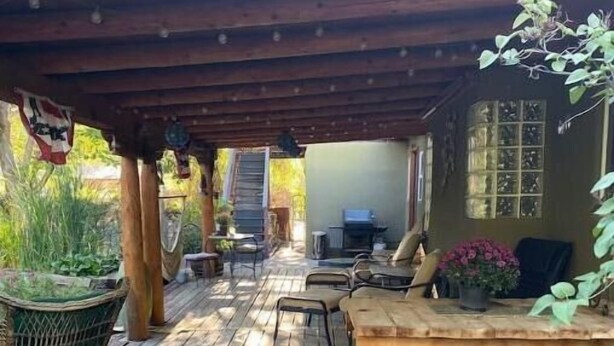 Una terraza de madera con un espacio cubierto, mobiliario exterior y una pequeña mesa.