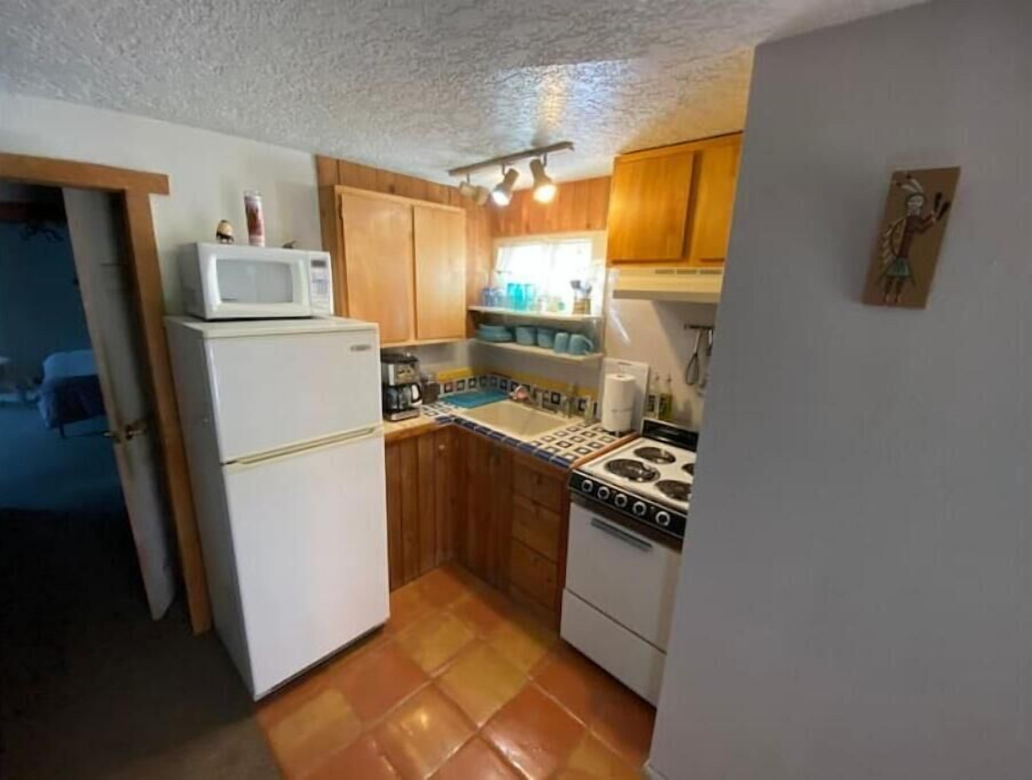 A compact kitchen with wooden cabinets, a white refrigerator, a stove, and a microwave.