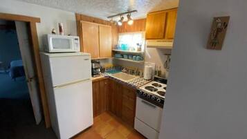 A compact kitchen with wooden cabinets, a white refrigerator, a stove, and a microwave.
