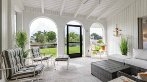 A covered patio with a view of a canal, featuring a sofa, chairs, and a dining table.