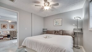 Ein Schlafzimmer mit einem großen Bett, einem Deckenventilator, einem Nachttisch mit Lampe und einem gerahmten Bild an der Wand.