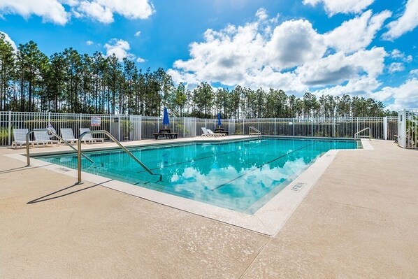 A rectangular swimming pool with a metal fence, lounge chairs, and a clear sky.