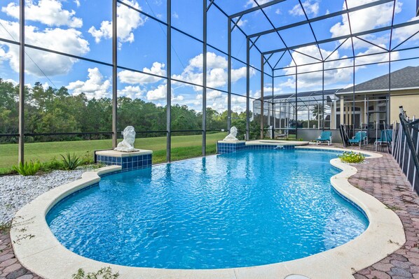 A swimming pool with two statues, surrounded by a covered area with chairs and a view of a house and trees.