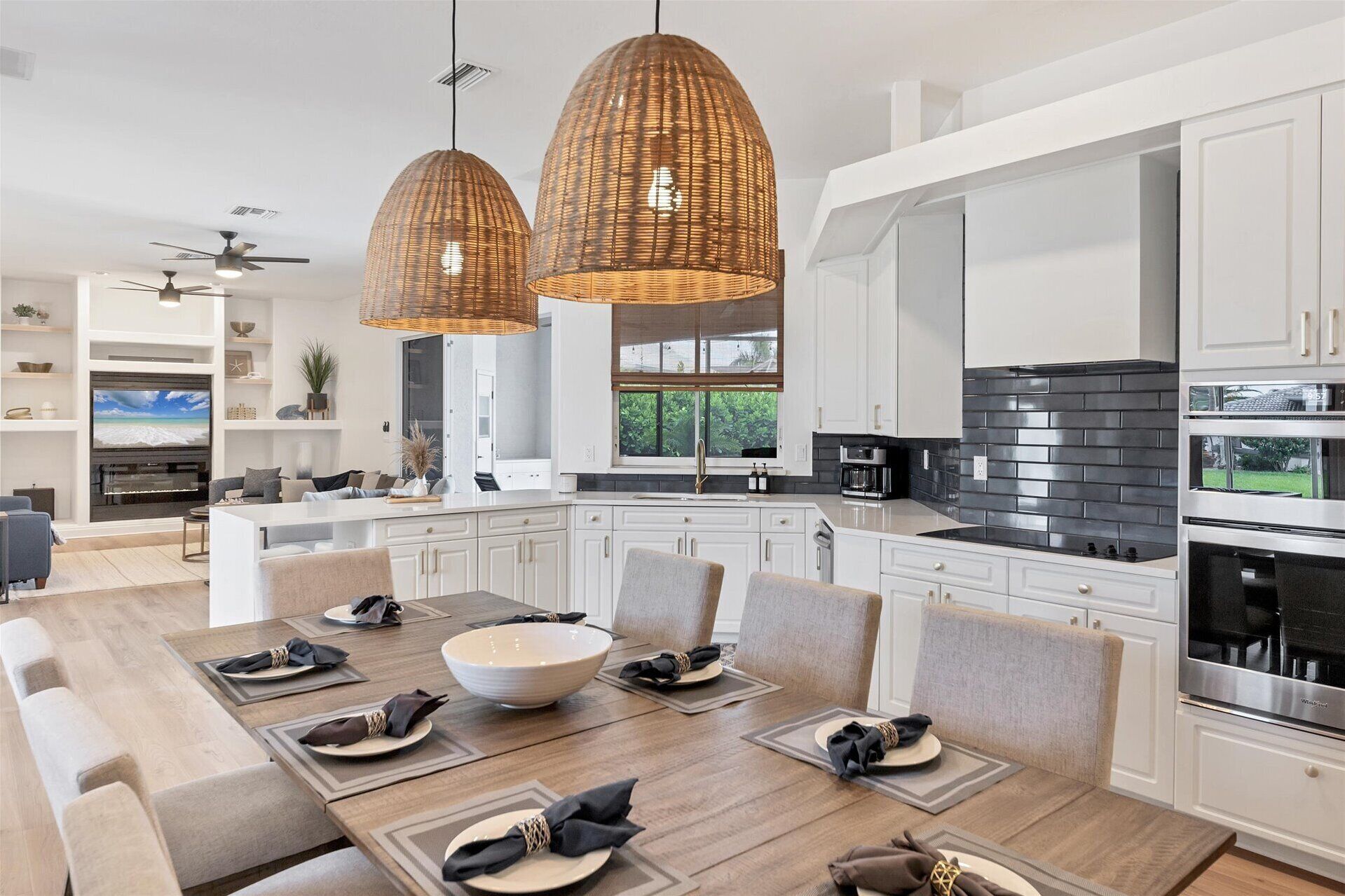 A modern kitchen with white cabinetry, a black tiled backsplash, and a dining area with a large table set for six.
