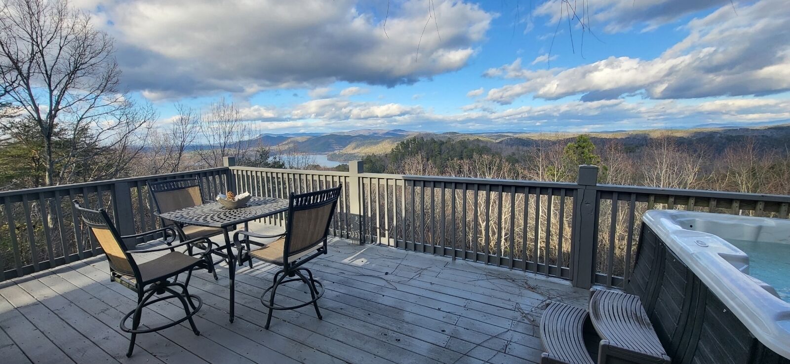 Een houten terras met een tafel, stoelen, een hottub en een prachtig uitzicht op bergen en een meer.