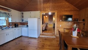 A wooden cabin with a kitchen featuring white cabinets, a refrigerator, a coffee maker, and a dining area with a table and chairs. - Lake View Cabin in ranger GA 4 Bedrooms (Ranger)