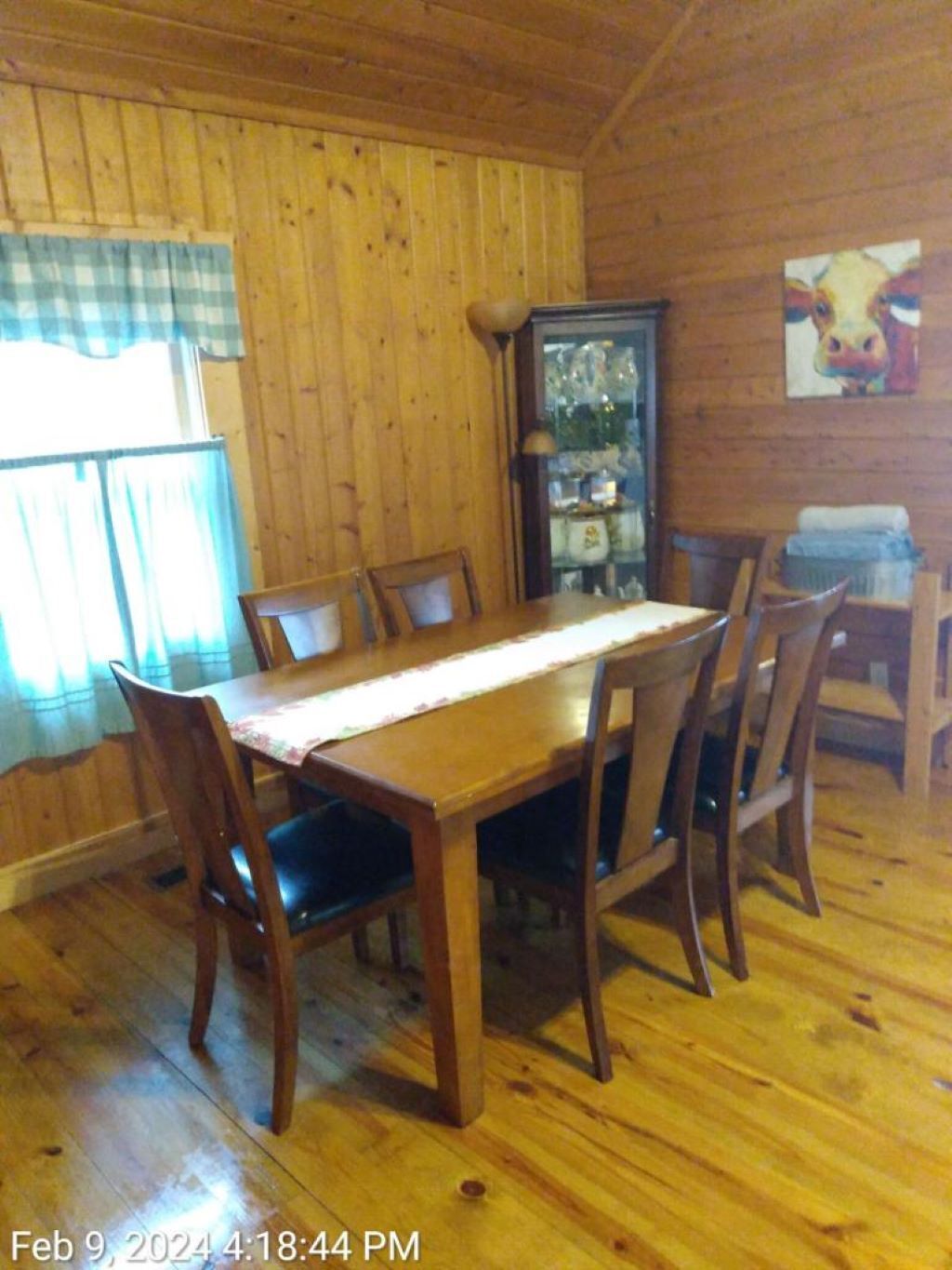 A wooden dining room with a table and chairs, a cabinet, and a painting on the wall.