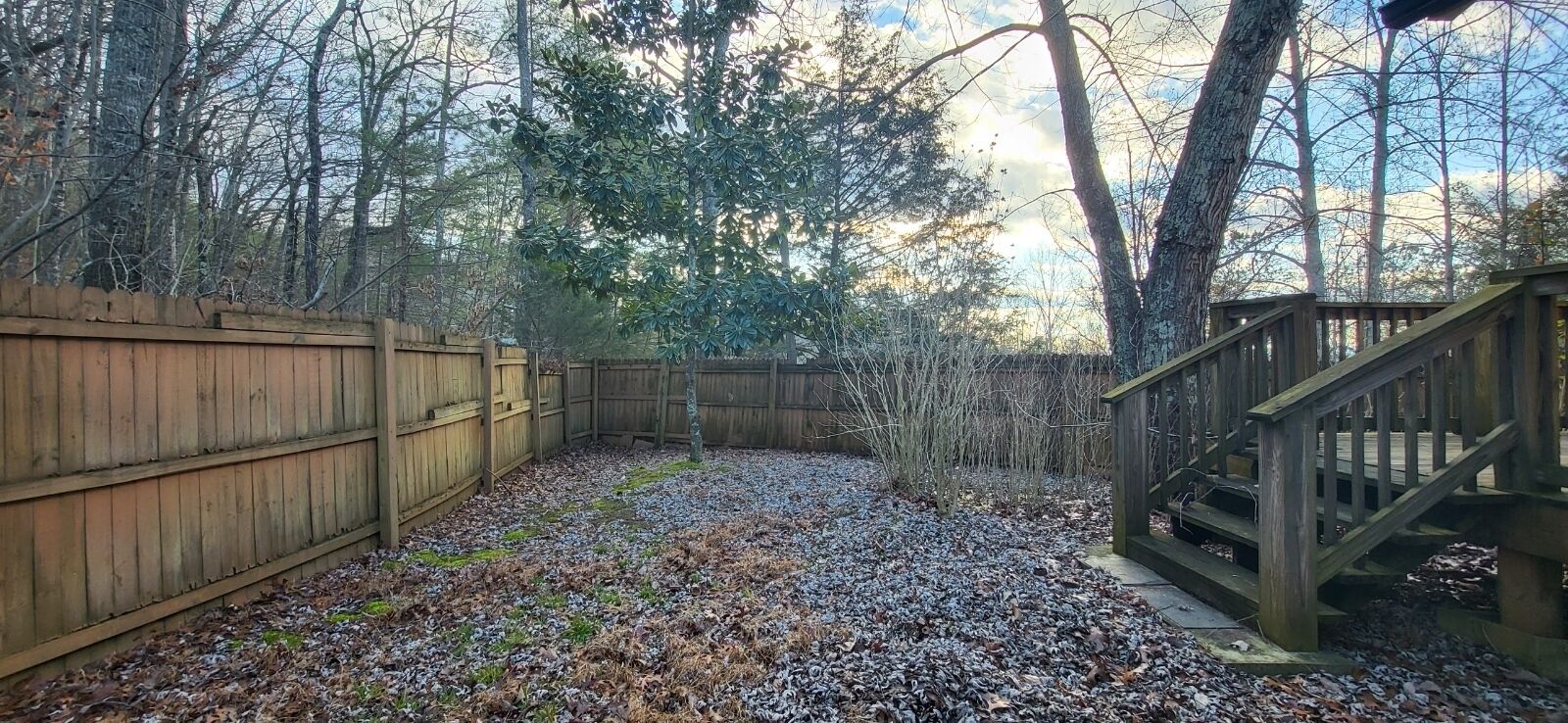 A fenced backyard with a wooden deck and stairs leading up to a raised platform.