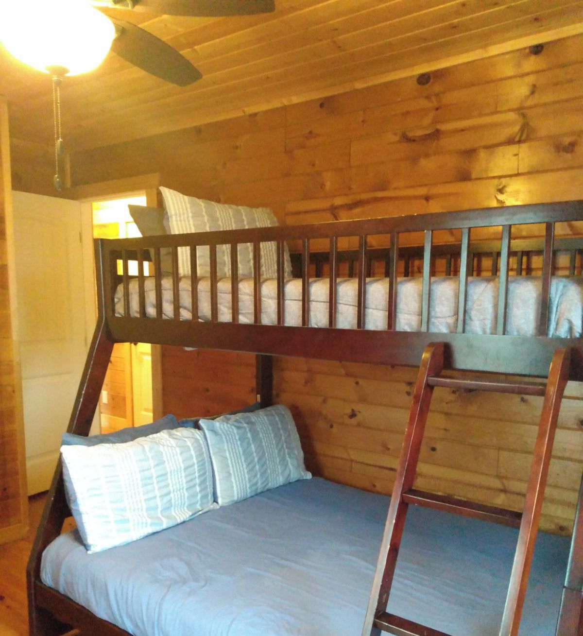 A bunk bed in a wooden cabin room with a ceiling fan and a window.