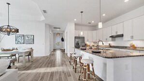 A modern kitchen with white cabinetry, a large island with stools, and a dining area with a wooden table and chairs. - New Listing! Charlotte Harbor Area Resort, 120mi to Disney & 134mi to Universal - GRH575527 (Punta Gorda)