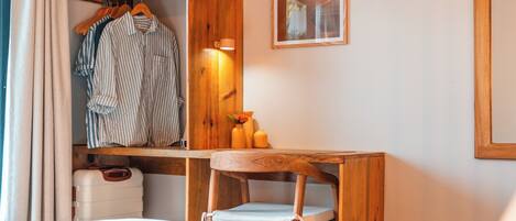 A hotel room with a wooden desk, a chair, a bed, a wardrobe, and a framed picture on the wall.