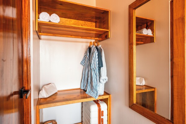 Un estante de madera con toallas y una maleta, un espejo que refleja el estante, y una puerta de madera.