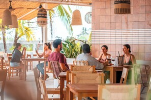 A restaurant with wooden tables and chairs, hanging wicker lamps, and a view of palm trees. - Bambuda Santa Catalina (Hicaco)
