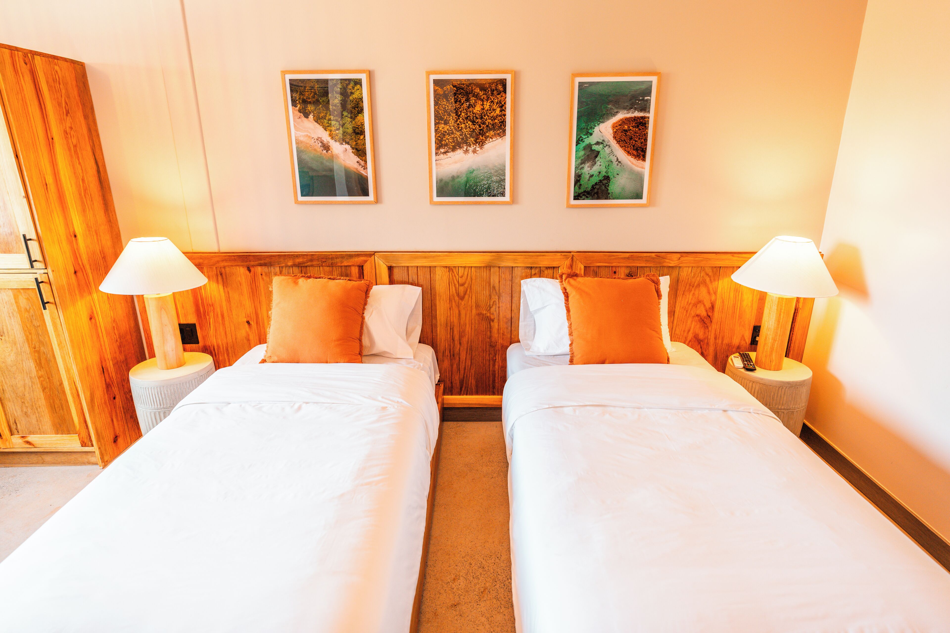 Habitación de hotel con dos camas, cabecero de madera, ropa de cama blanca y tres cuadros en la pared.