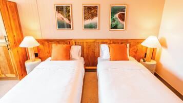 Habitación de hotel con dos camas, cabecero de madera, ropa de cama blanca y tres cuadros en la pared.