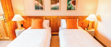 A hotel room with two beds, wooden headboard, white bedding, and three framed pictures on the wall.