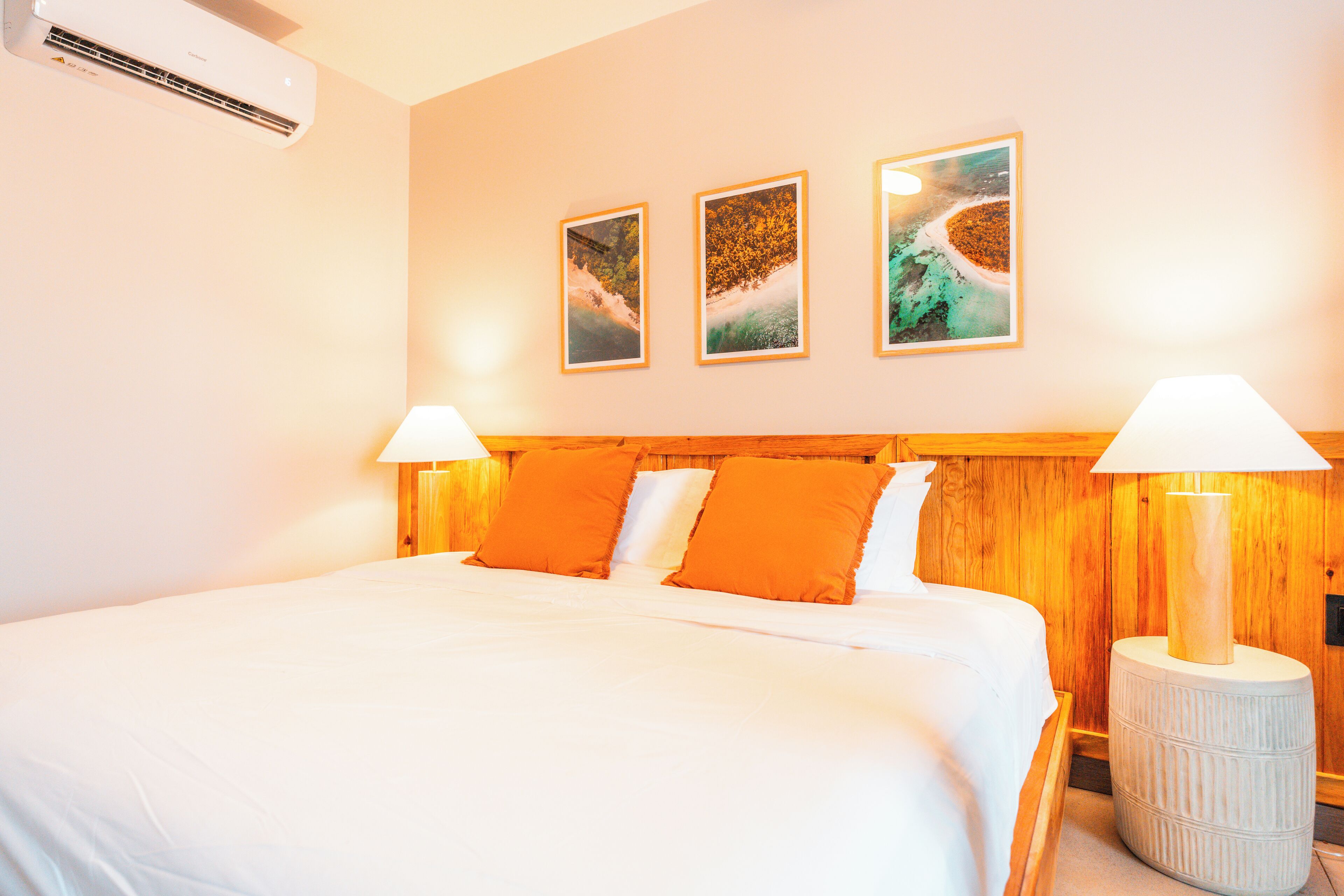 Ett hotellrum med en stor säng, ett träbeklätt sänggavel, två sänglampor och tre inramade tavlor på väggen.