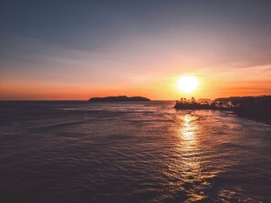 A sunset over a calm sea with a distant landmass. - Bambuda Santa Catalina (Hicaco)
