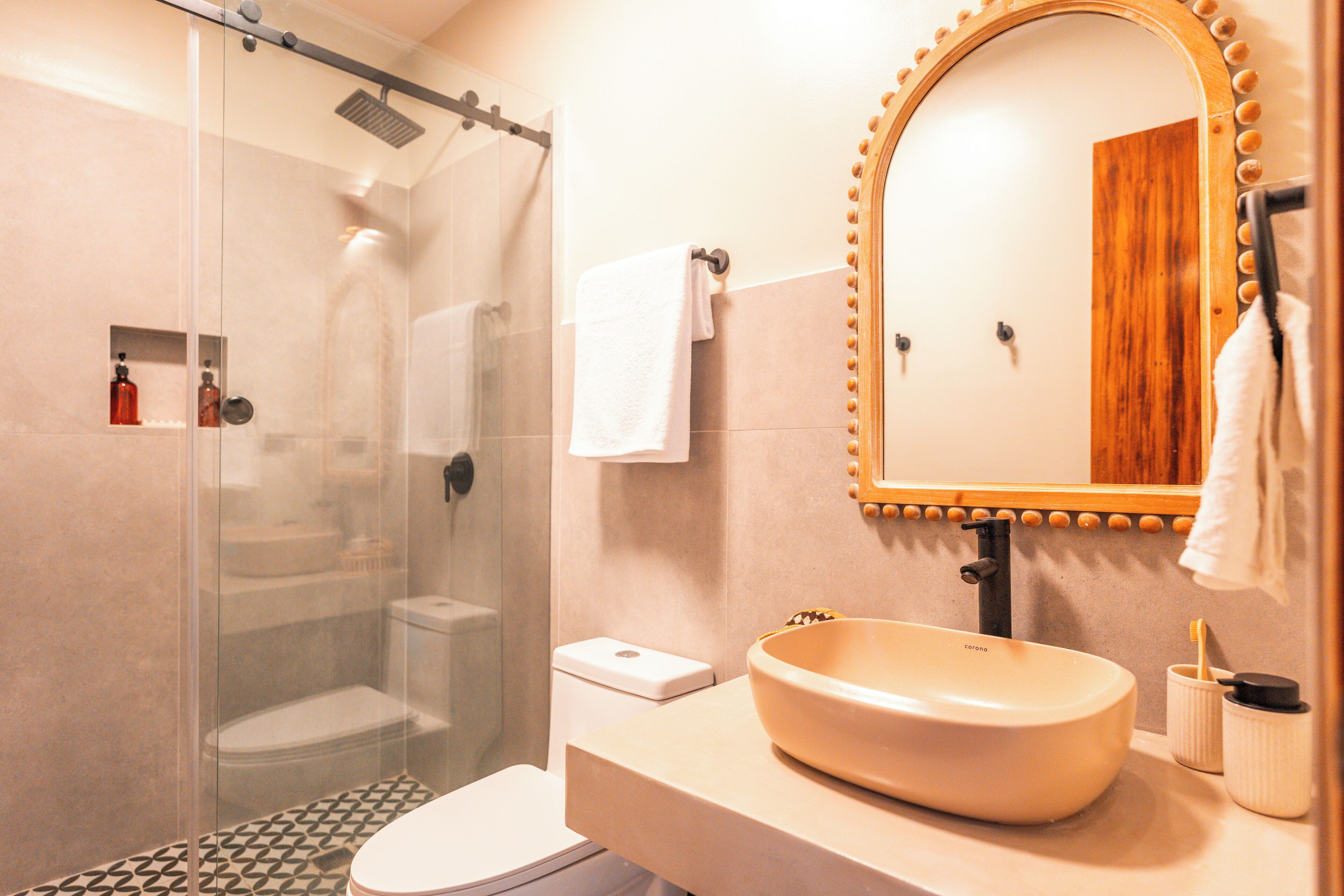 Un baño con ducha envuelta en vidrio, un lavabo con tocador de madera y un espejo con marco de madera.