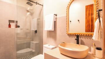 Un baño con ducha envuelta en vidrio, un lavabo con tocador de madera y un espejo con marco de madera.