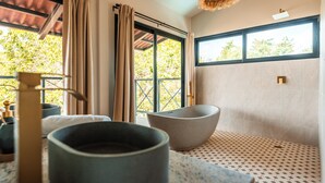 Un baño con un ventanal grande, una lámpara colgante y dos grandes cuencos en el suelo.