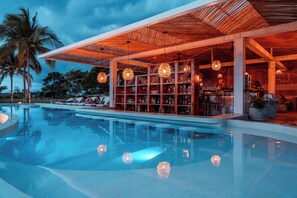 A modern poolside area with a bar and lounge seating, surrounded by palm trees. - Bambuda Santa Catalina (Hicaco)
