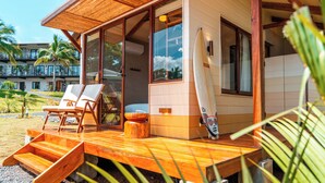 Una terraza de madera con una tabla de surf apoyada en la pared, una silla y una pequeña mesa.