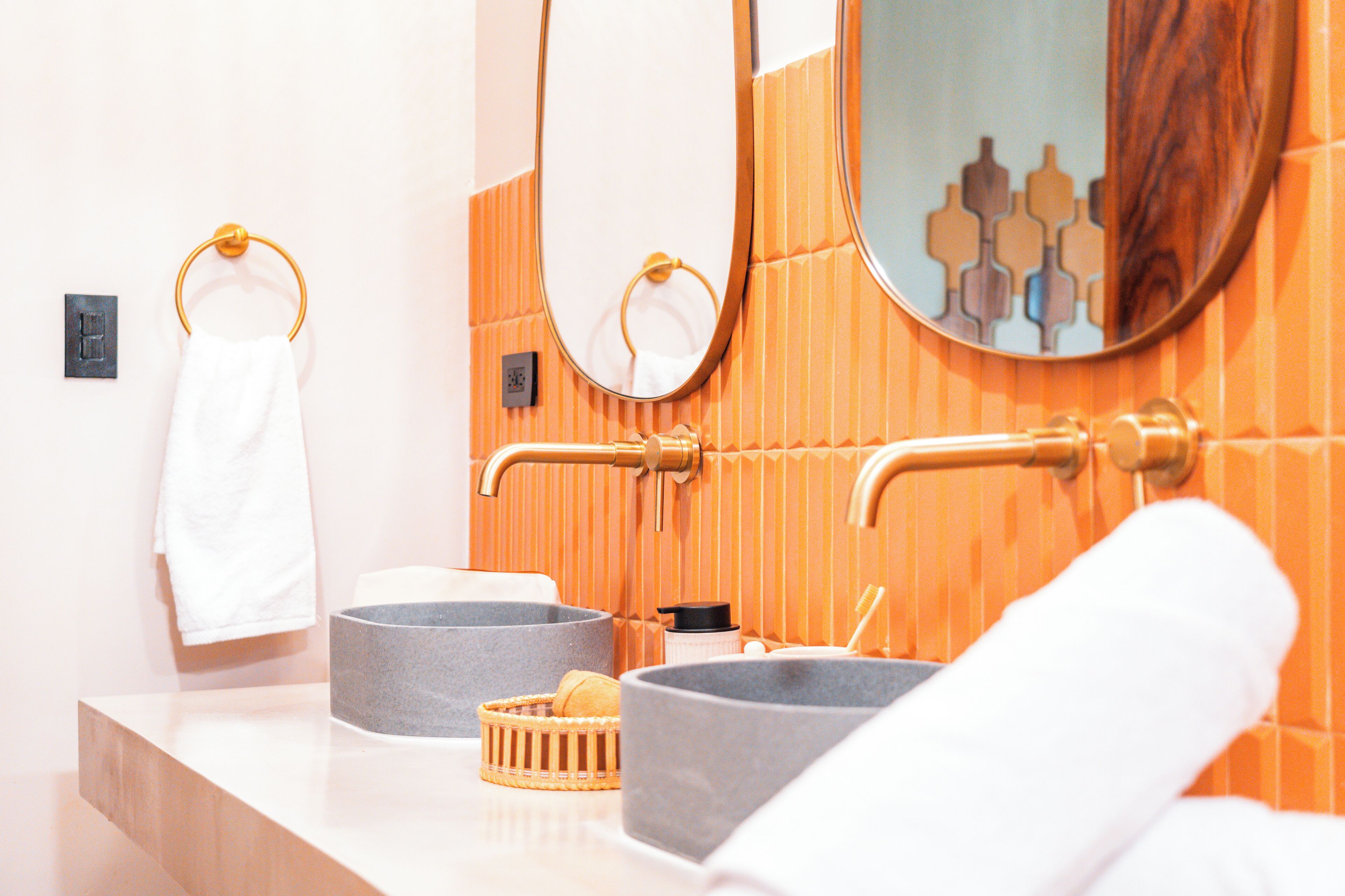 A bathroom with a white countertop, two grey bowls, a wooden basket, and a white towel.