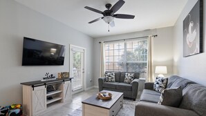 A living room with a flat-screen TV, a ceiling fan, a sofa, a coffee table, and a TV stand. - New Listing! Windsor Hills Resort, 3mi to Disney & 12mi to Universal - GRH802721 (Kissimmee)