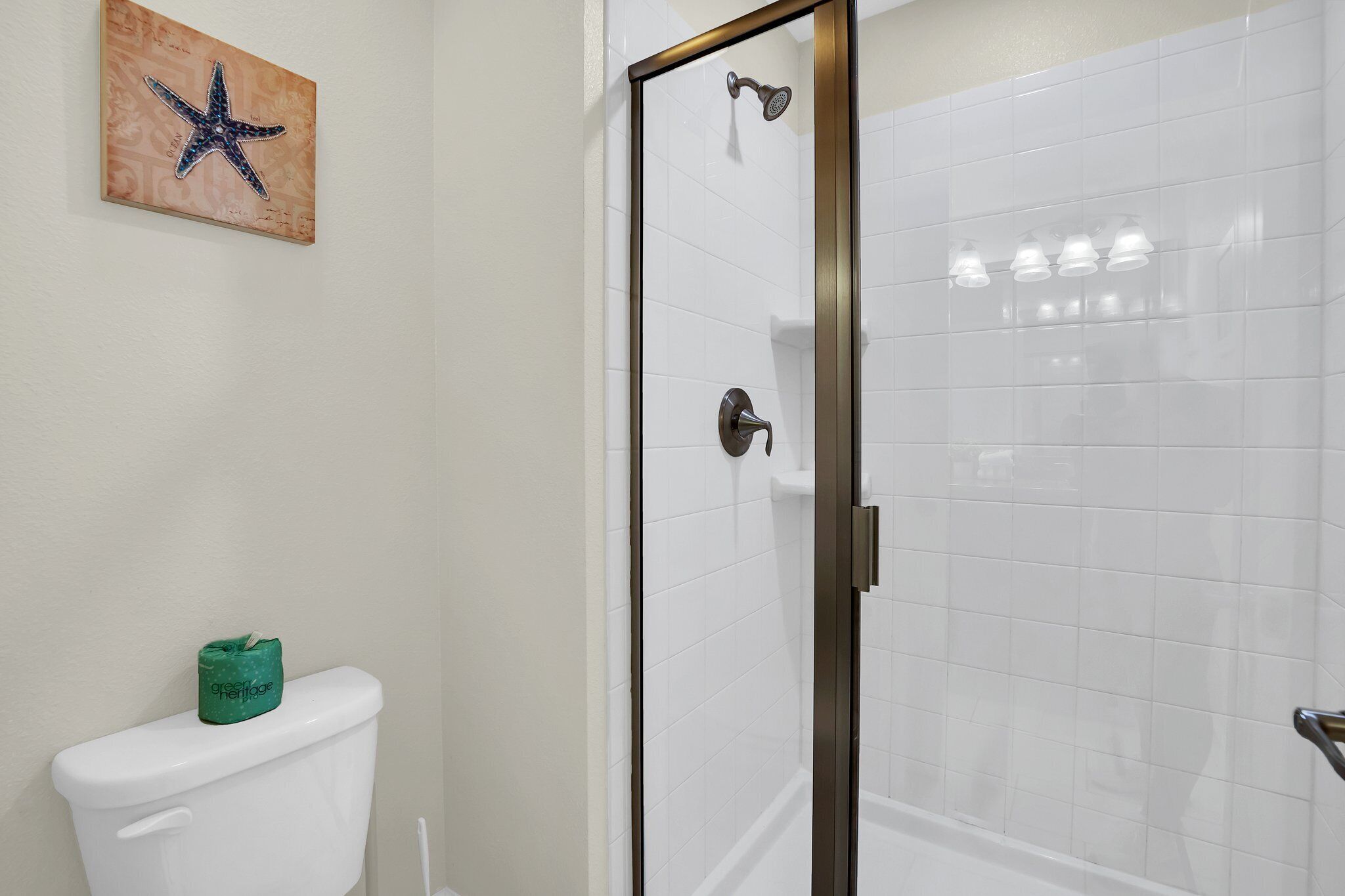 A bathroom with a toilet, a shower with a glass door, and a starfish artwork on the wall.