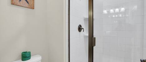 A bathroom with a toilet, a shower with a glass door, and a starfish artwork on the wall.