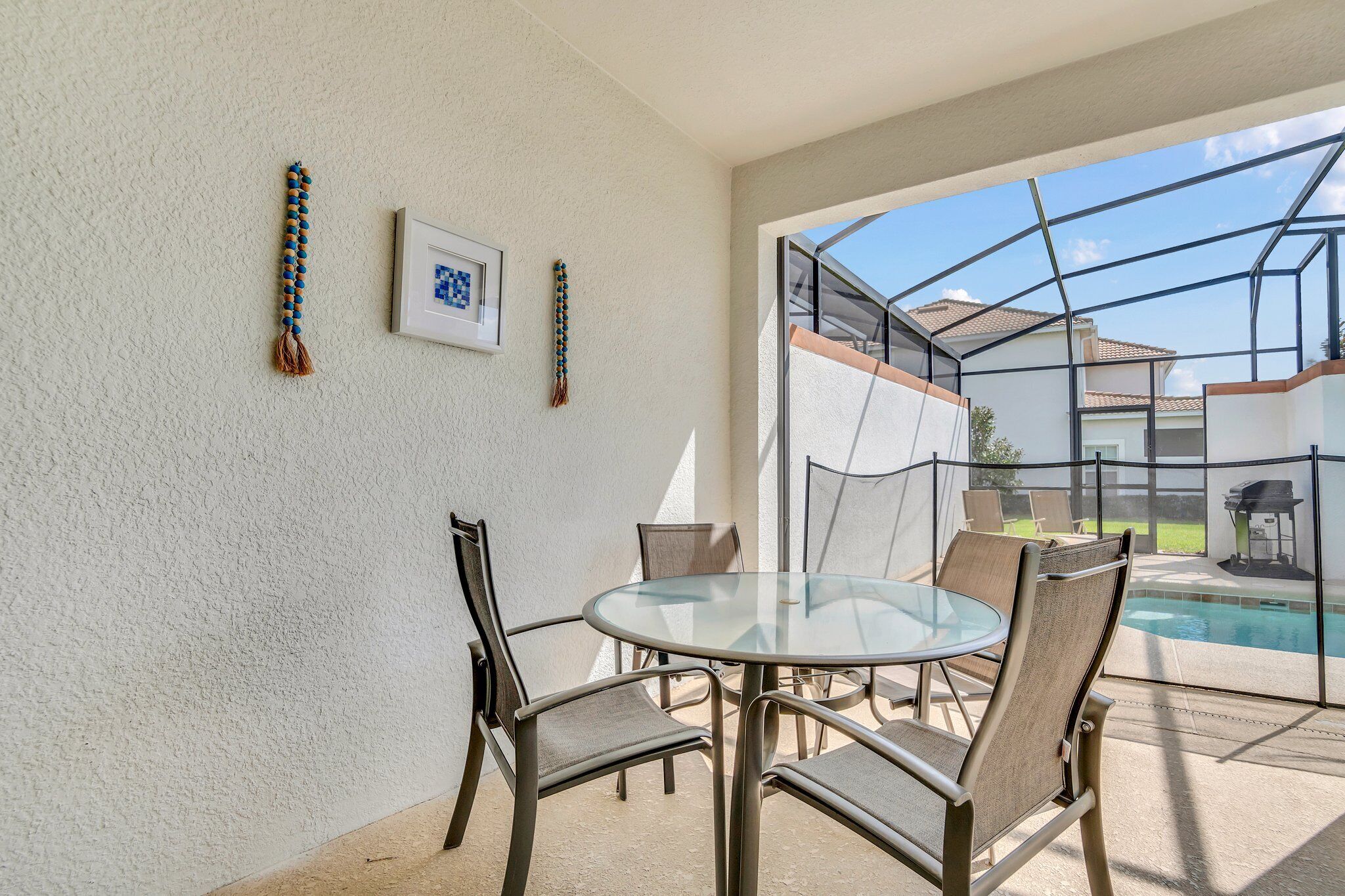 Een glazen patio met een ronde tafel en stoelen, een zwembad en een uitzicht op een huis op de achtergrond.