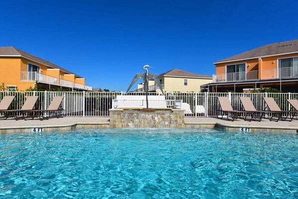 A swimming pool with lounge chairs and a statue in the center, surrounded by buildings.