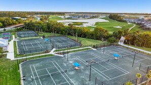 Vista aérea de un complejo deportivo con canchas de tenis, campo de golf y zona de estacionamiento.