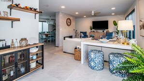 A modern living room with a sofa, ottomans, a coffee table, and a TV. There are shelves with decorative items and a ceiling fan. - Spacious 4BR with rooftop deck – ocean views & beach access (Seaside Heights)