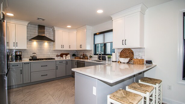 A modern kitchen with white cabinets, a large island with bar stools, stainless steel appliances, and a window providing natural light. - Spacious 4BR with rooftop deck – ocean views & beach access (Seaside Heights)