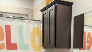 Un baño con cortina de ducha que muestra letras grandes y coloridas, un inodoro, un lavamanos con espejo y armarios oscuros.