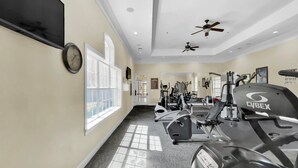 Un gimnasio con ventiladores de techo, equipo de ejercicio y amplias ventanas.