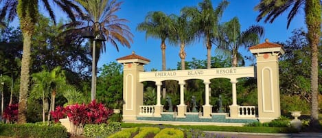 A resort entrance with a sign reading 'Emerald Island Resort' surrounded by palm trees and landscaped gardens.
