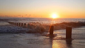 A sunset over the ocean with waves crashing onto a sandy beach and wind turbines in the distance. - Beautiful 2 Bed Caravan Southview Park Skegness (Skegness)
