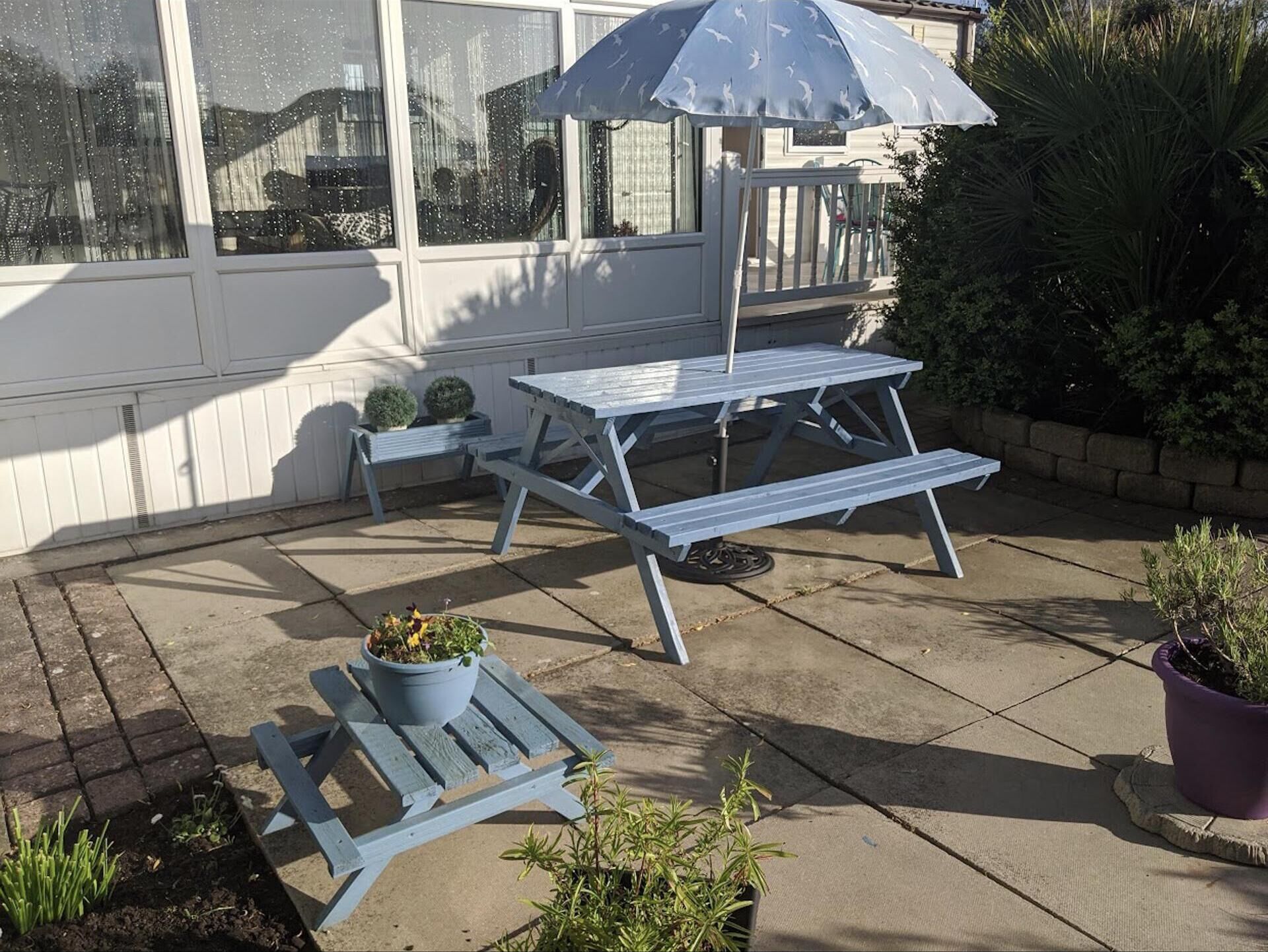 A patio with a picnic table and benches, surrounded by potted plants and a small garden area.