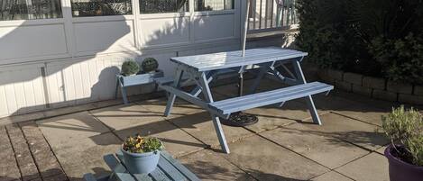 A patio with a picnic table and benches, surrounded by potted plants and a small garden area.