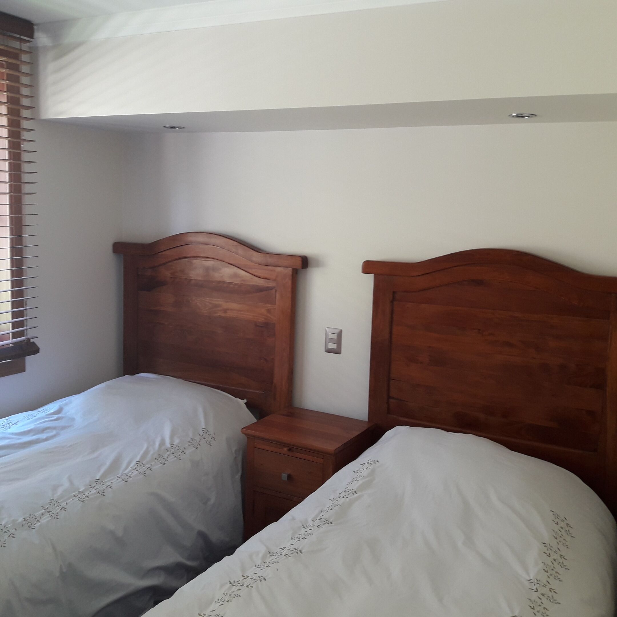 A bedroom with two wooden beds, a nightstand, and a window with blinds.
