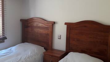A bedroom with two wooden beds, a nightstand, and a window with blinds.