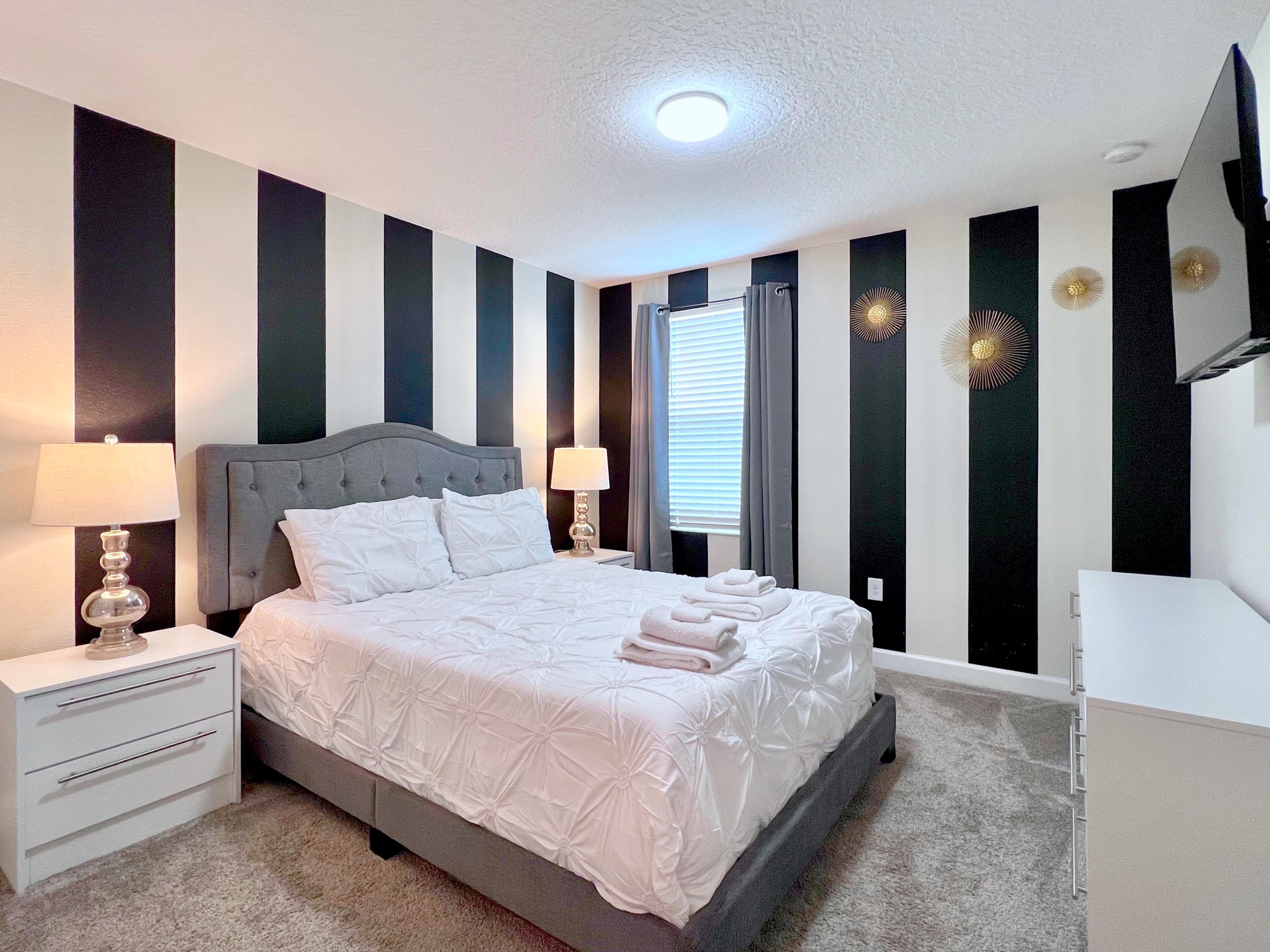 A neatly arranged bedroom with a bed, two bedside tables, a dresser, and a window with curtains.