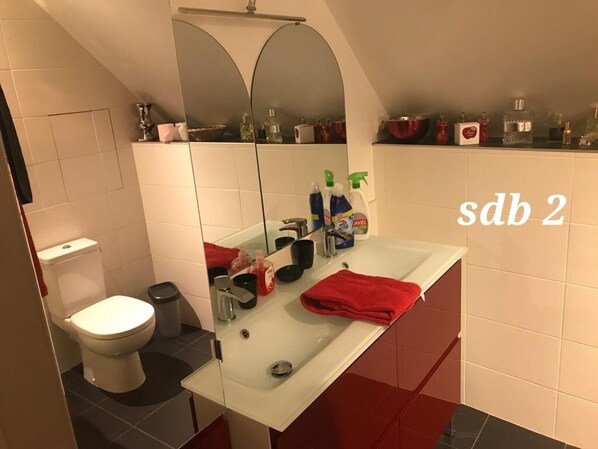 A modern bathroom with a white sink, red towels, and toiletries on the counter.