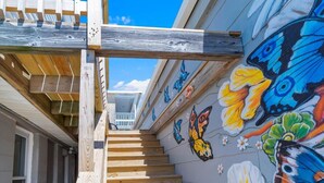 A wooden staircase leading to a balcony with a colorful mural of butterflies and flowers. - Oceanfront Escape Just Steps to Beach & Boardwalk , beach badges 2 car park (Seaside Heights)