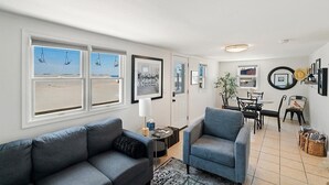 A living room with a view of the beach, a dining area with a table and chairs, and a sofa. - Oceanfront Escape Just Steps to Beach & Boardwalk , beach badges 2 car park (Seaside Heights)