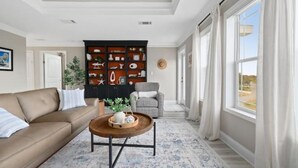 Una sala de estar con un sofá marrón, una mesa de centro, una estantería y vistas amplias a través de grandes ventanales.